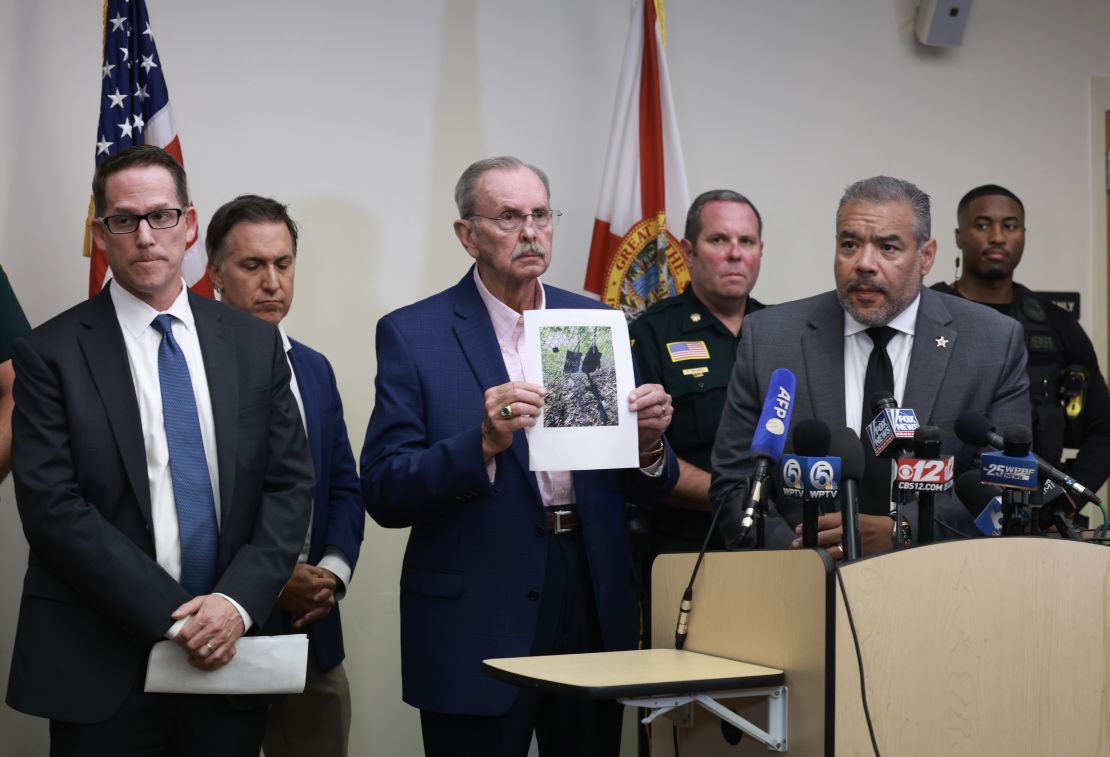 Palm Beach County Sheriff Ric Bradshaw, center, holds a photograph of the rifle and other items found near where a suspect was discovered on September 15, 2024, in West Palm Beach, Florida.